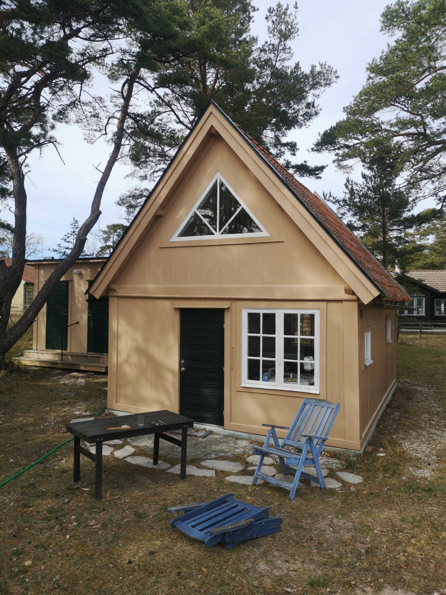 Gaveln på ett sandfärgat hus med brant sluttande tak, dörren står öppen, vita fönster, varav ett trekantigt ovan dörren.